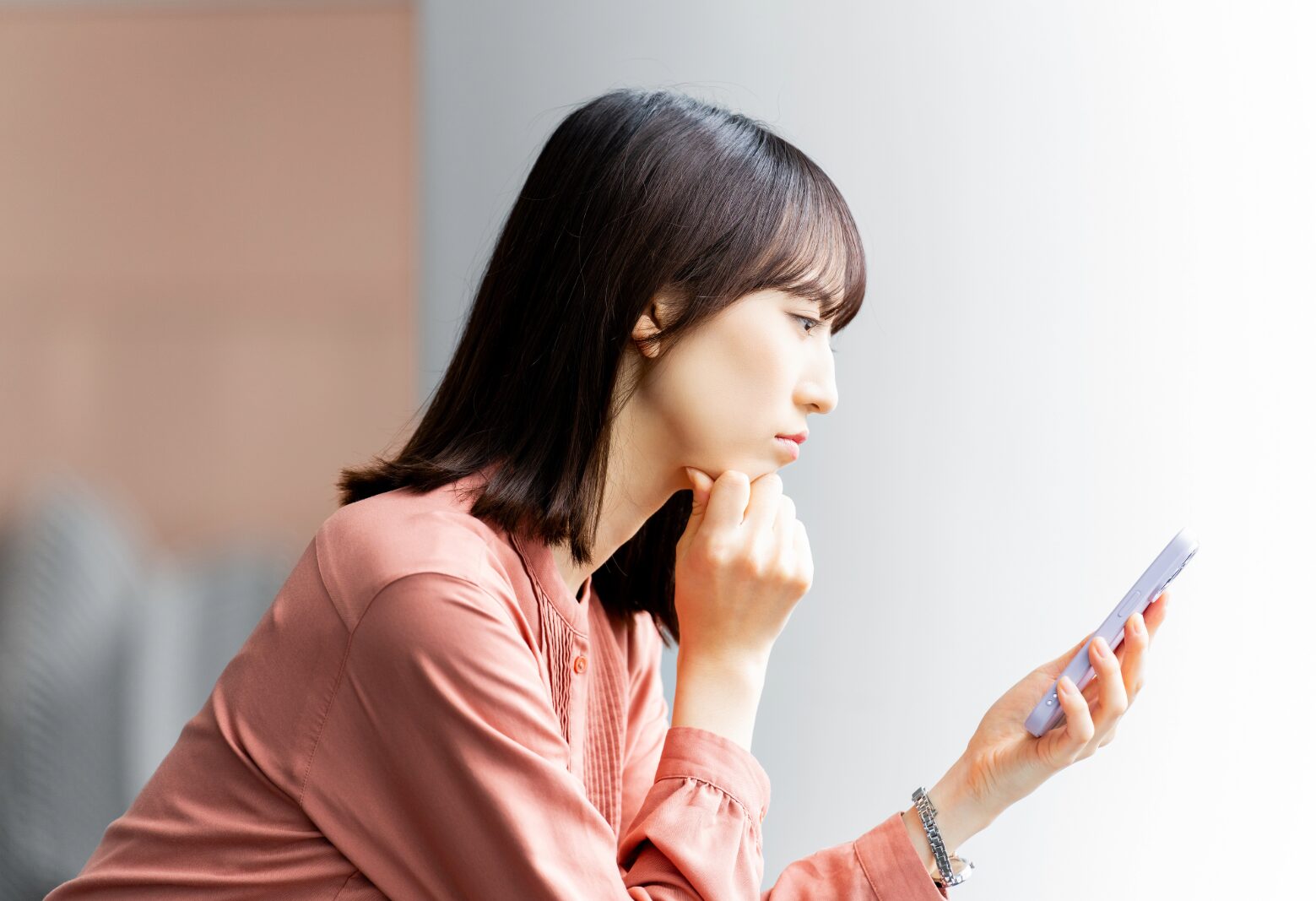 スマホを持って少し考えている女性 申し込みボタンを押すか迷っている女性